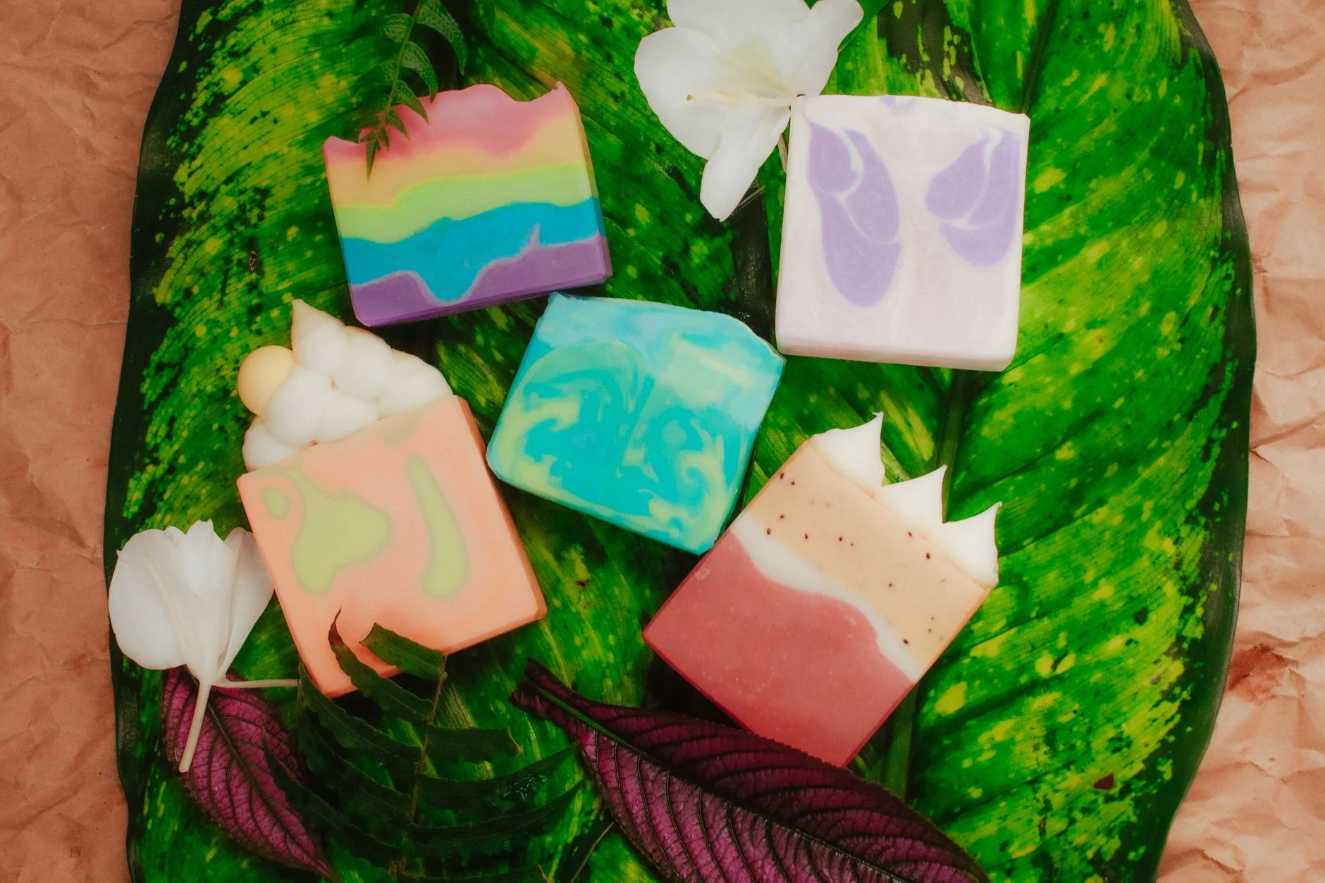 Vibrant handmade soaps displayed on lush green leaves with floral accents, perfect for eco-friendly themes.
