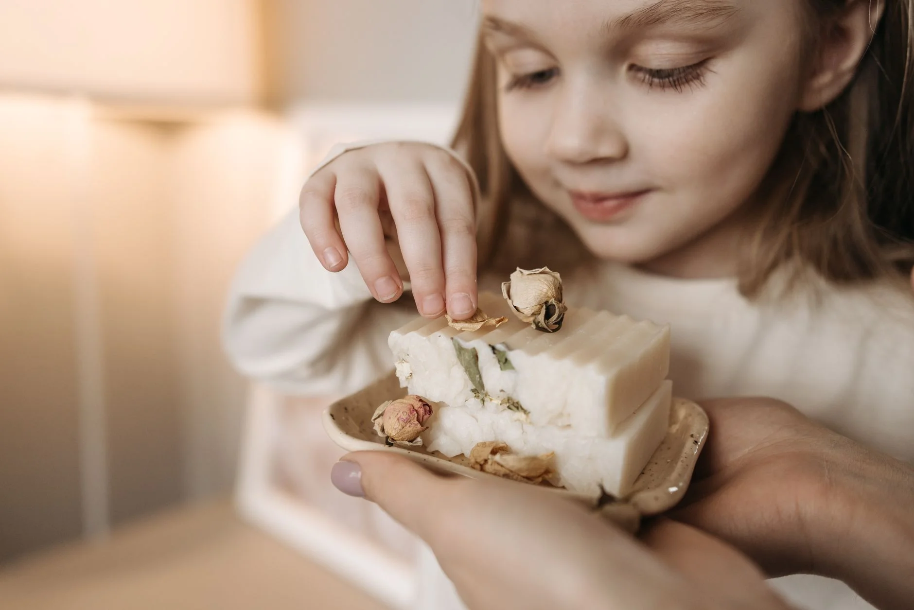 A smiling child appreciates a handcrafted soap with dried flowers in a warm, cozy setting.