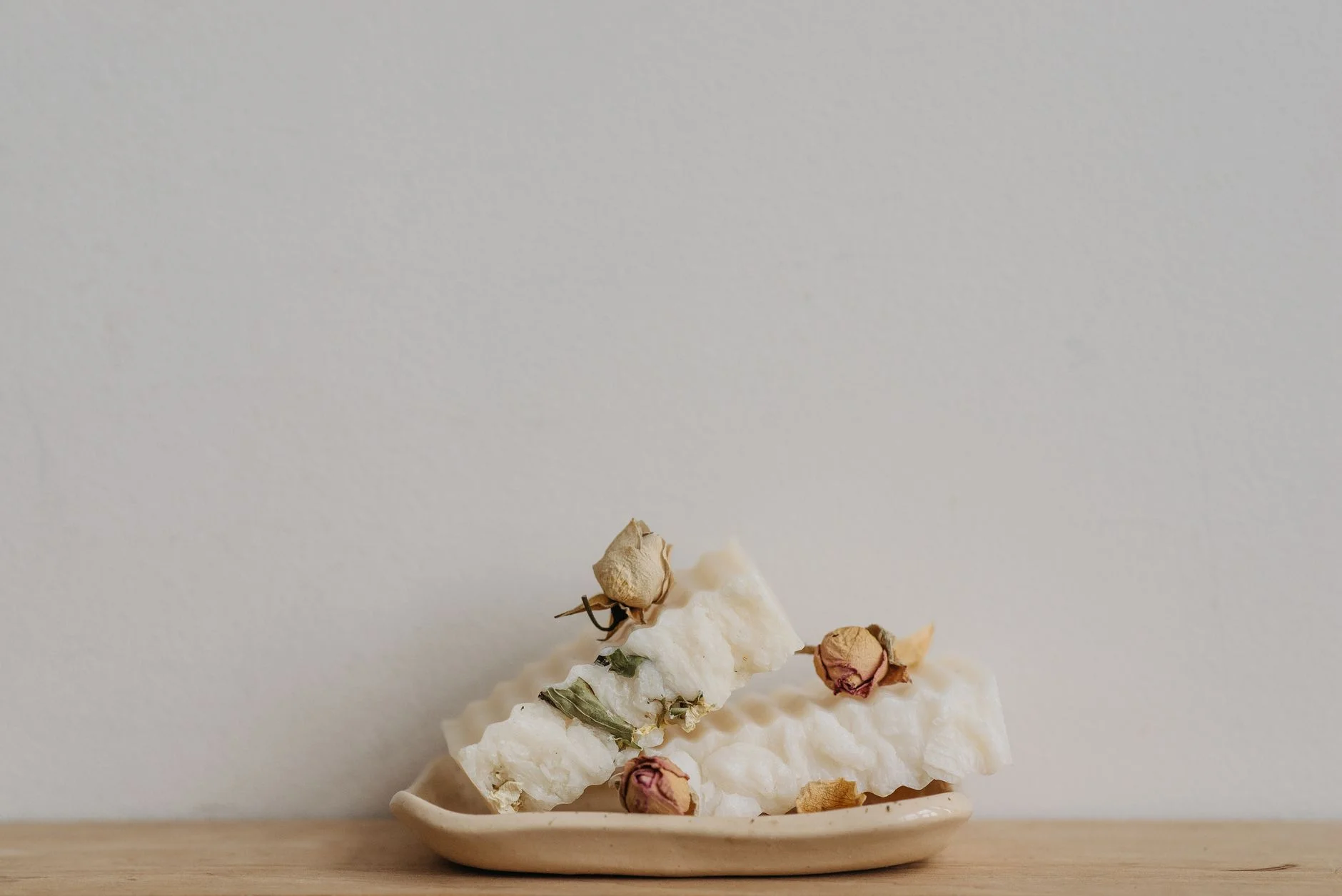 Eco-friendly white soap bars with dried flowers on a ceramic tray, perfect for sustainable living.